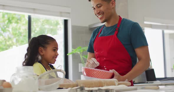 Happy biracial father and daughter baking together in kitchen