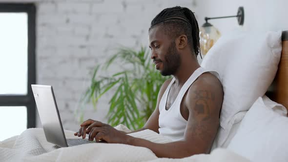 Side View of Concentrated Handsome Tattooed African American Man Typing on Laptop Keyboard in Slow