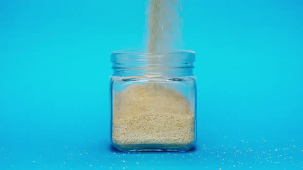 Closeup of Falling Down Quinoa Into Glass Jar on Blue Background