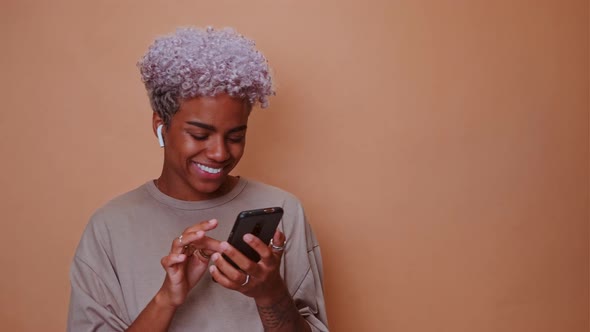 Young African American Woman with Phone Listening Music Via Bluetooth Earphone