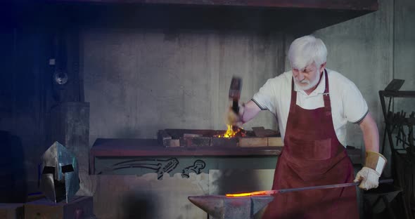 Old Man in Red Arpon and Gloves Forging in Smithy