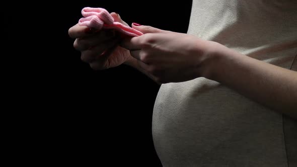 Pregnant Woman Holding Pink Socks Isolated on Black, Anxious About Baby Health