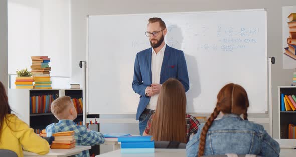 Male Teacher Teaching How to Count Standing Near Whiteboard in Classroom