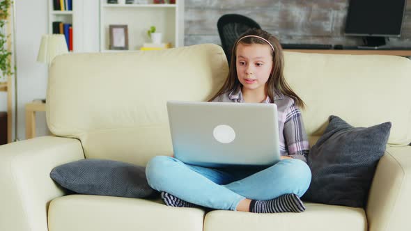 Sweet Little Girl with Braces Sitting on the Couch Using Her Laptop