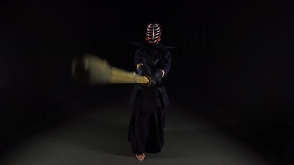 Strong Kendo Guru Practicing Martial Art with the Bamboo Bokken on Black Background.