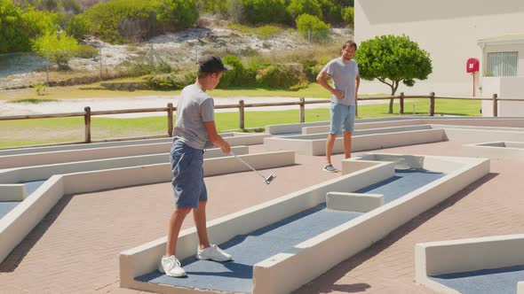 Man with His Son Playing Mini Golfers on Mini Golf Course at Summer Day