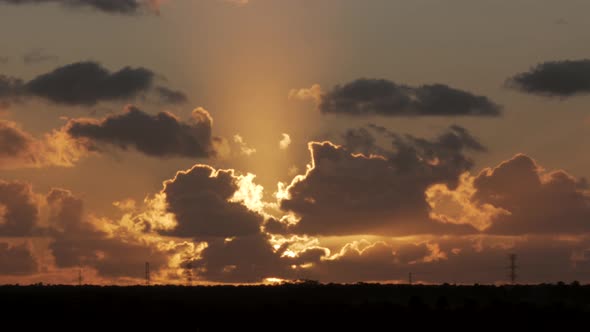 Static wide shot of gigantic golden sunset lights shining behinding clouds silhouette at horizon.