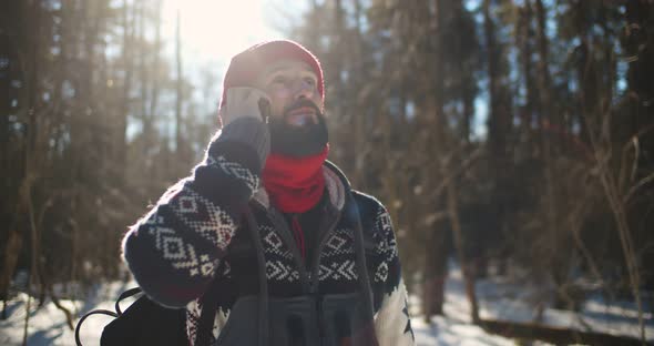 Man Traveler with Backpack Hiking in Winter Forest and Having Phone Call