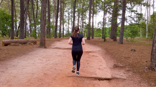 Girl running on a dirt trail between trees, camera following the subject from behind.