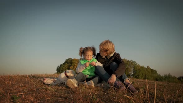 Woman with Little Daughter and Pet Dog Sitting During Amazing Sunset