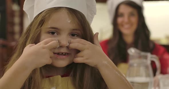 Close-up Face of Cheerful Little Caucasian Girl Drawing Lines on Face with Flour and Winking