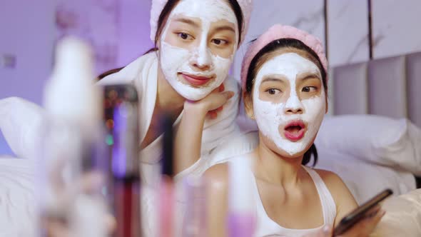Beautiful young woman in white bathrobe applying a revitalizing  mask her friend's face