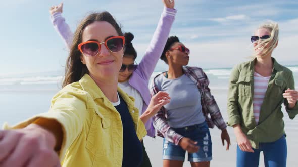 Happy group of diverse female friends having fun, dancing and smiling at the beach