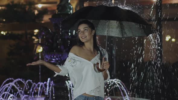 Attractive Woman Poses with Umbrella Under Flowing Fountain in Deep Evening