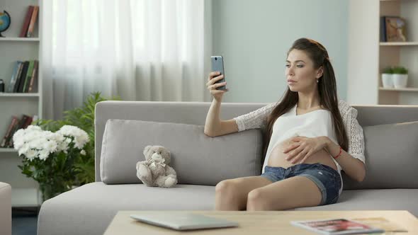 Female Pregnant With Child Sitting on Sofa and Using Mobile Phone, Online Blog