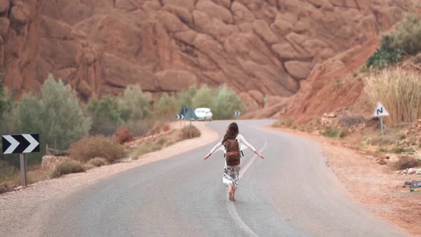 Woman walking away in the middle of the road with open arms at a desert canyon arid environment with