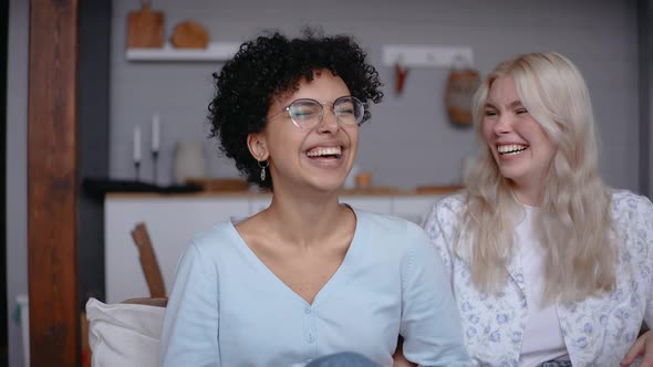 Beautiful Lesbian Couple Laugh Together Sitting on a Couch at Home