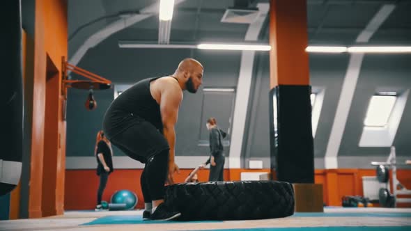 A Bearded Man Bodybuilder Flips a Tire on the Floor Over and Over in the Gym - Another People