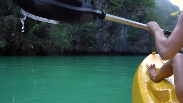 Woman paddles yellow kayak in the lake with turquoise water. 