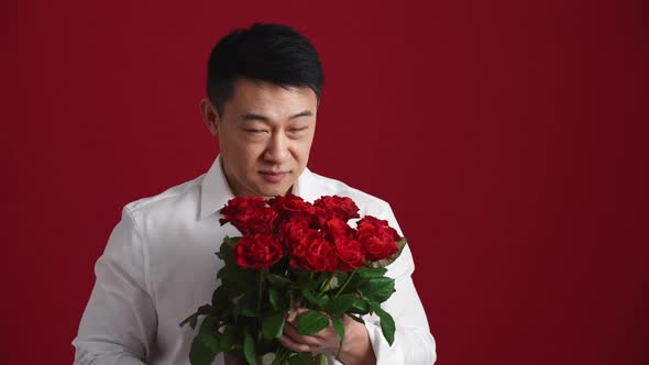 Positive Asian man in white shirt holds out a bouquet of red roses to the camera