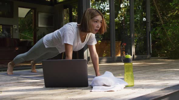 Asian woman practicing yoga outdoors in garden with laptop