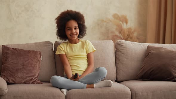 Portrait Little African American Girl Watches TV and Switches Channels with Interest with Remote