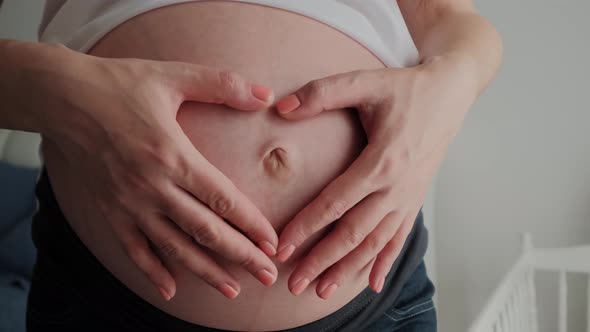Close Up Shot of Young Pregnant Woman Stroking Big Belly on Couch and Making Heart Shape with Hands
