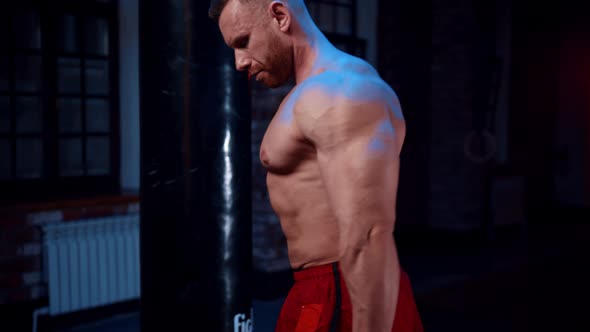 Strong Man Standing in the Gym and Pumping His Hands with Dumbells