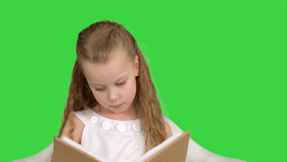 Pretty Little Girl Sitting with Book and Reading on a Green Screen, Chroma Key