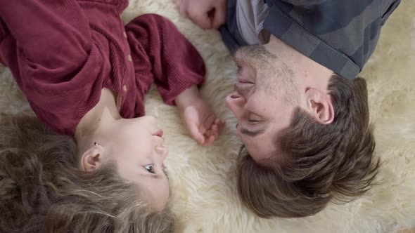 Faces of Positive Relaxed Man and Little Girl Lying on Soft Carpet Talking