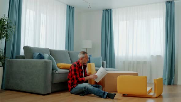 A Man Sitting on the Floor Near the Sofa is Studying the Instructions for Assembling the Chair