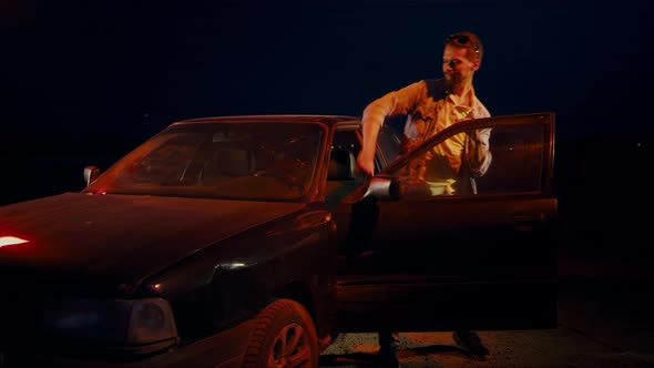 Man at Night Dances Jumps and Waves His Hands Near the Car with the Door Open