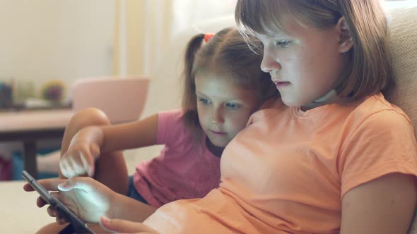 Two Girls Children Sister At Home On Couch Playing On Tablet