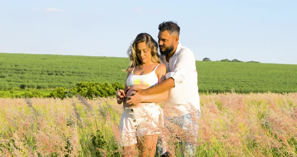 Loving couple waiting for baby, flowery field, lush nature, beautiful green background.