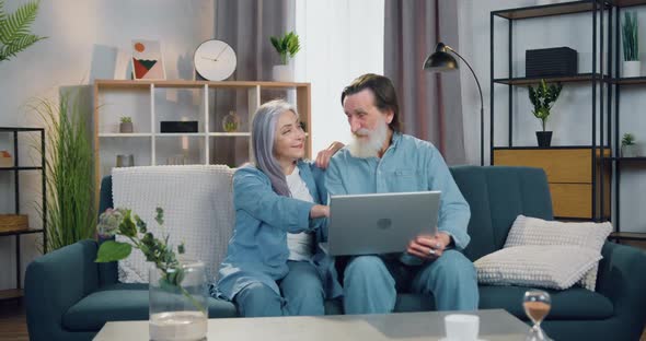 Senior Couple Resting on the Couch at Home and Discussing News they Had Read on Laptop Screen