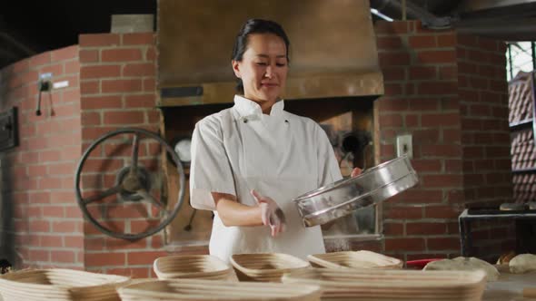 Animation of of happy asian female baker sieving flour on board