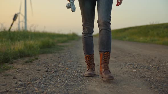 Young hiker with a camera walking along the road in the field