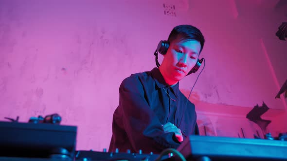 Modern DJ of Asian Appearance Performs a Music Track in Neon Lighting