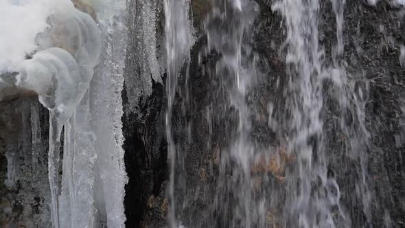 Spring meltwater cascading over frozen waterfall, winter mountain stream closeup