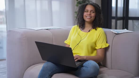 Portrait of Charming Happy African American Young Woman Sitting on Couch in Living Room Typing on