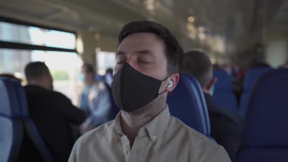Masked Caucasian Man in Black Protective Mask is Taking Nap in Train Listening to Music in Wireless