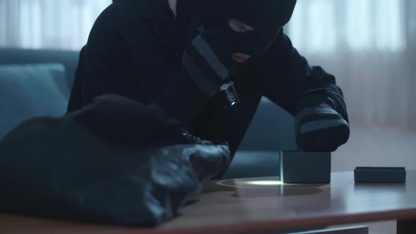 Close Up Of A Thief Man Holding Flashlight Stealing A Watch In Someone'S House Before Walking Away