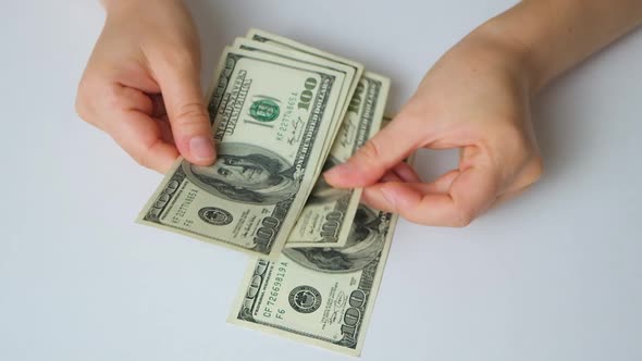 A Woman Counts Dollar Bills for 100 Dollars on a White Background Top View