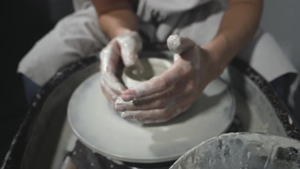 Potter molds clay pot on potter's wheel in workshop