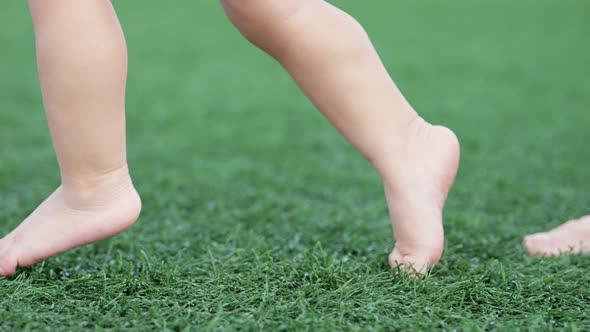 Toddler Learns Walking with Parents Help on Green Grass