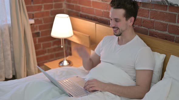 Young Man Doing Video Chat on Laptop in Bed