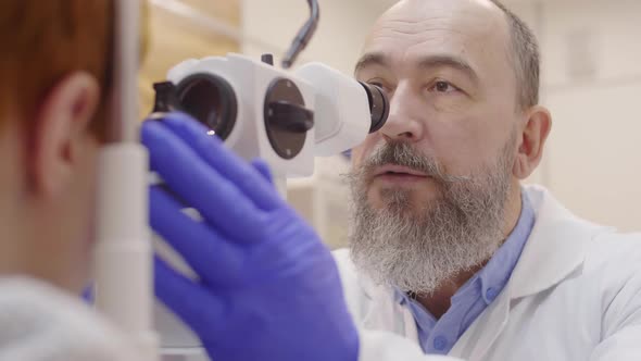 Mature Optometrist Giving Slit Lamp Eye Exam to Kid