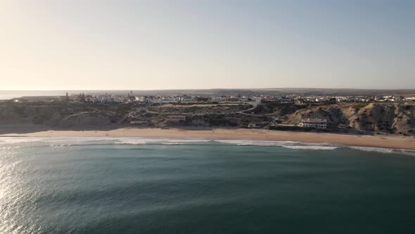 Aerial flying forward Sandy bay protected by rocky cliffs, Mareta Beach - Sagres