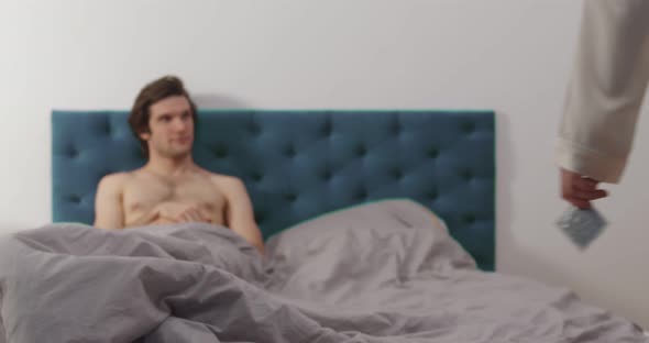 Attractive Woman Holding Condom Joining Handsome Man in Bed