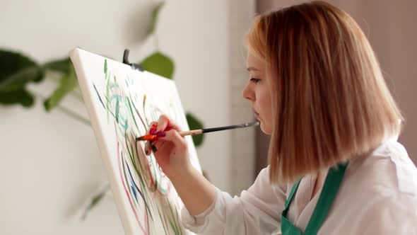 Woman Draws on Canvas with Brush Holding Palette of Paints in Hand Side View